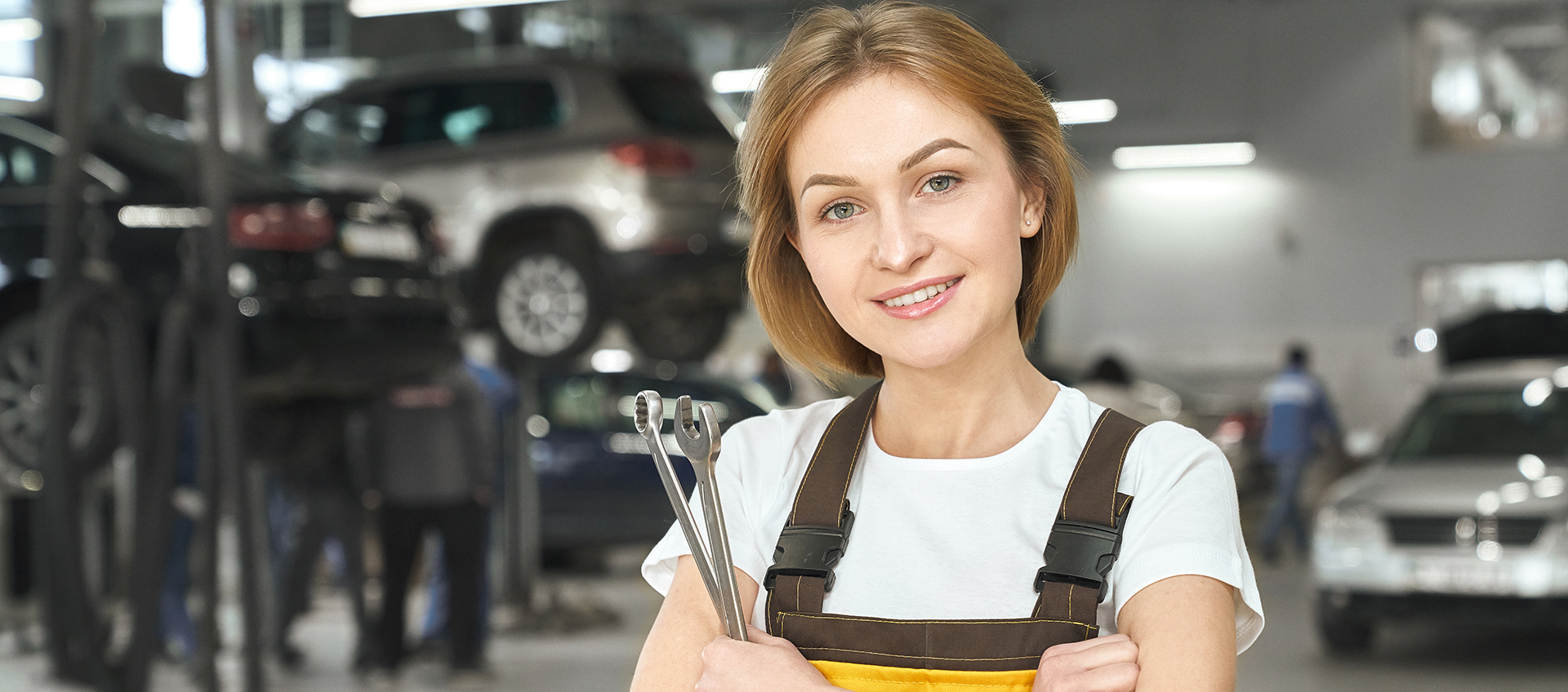 A female mechanic holds wrenches in a modern auto repair shop at Fahrzeugtechnik Nink. She is smiling and ready to provide quality vehicle service.