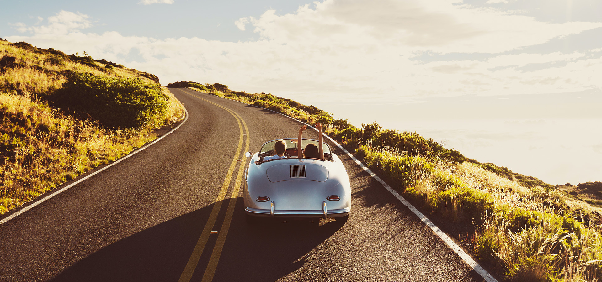 Couple enjoying a scenic drive in a classic convertible on a winding road.
