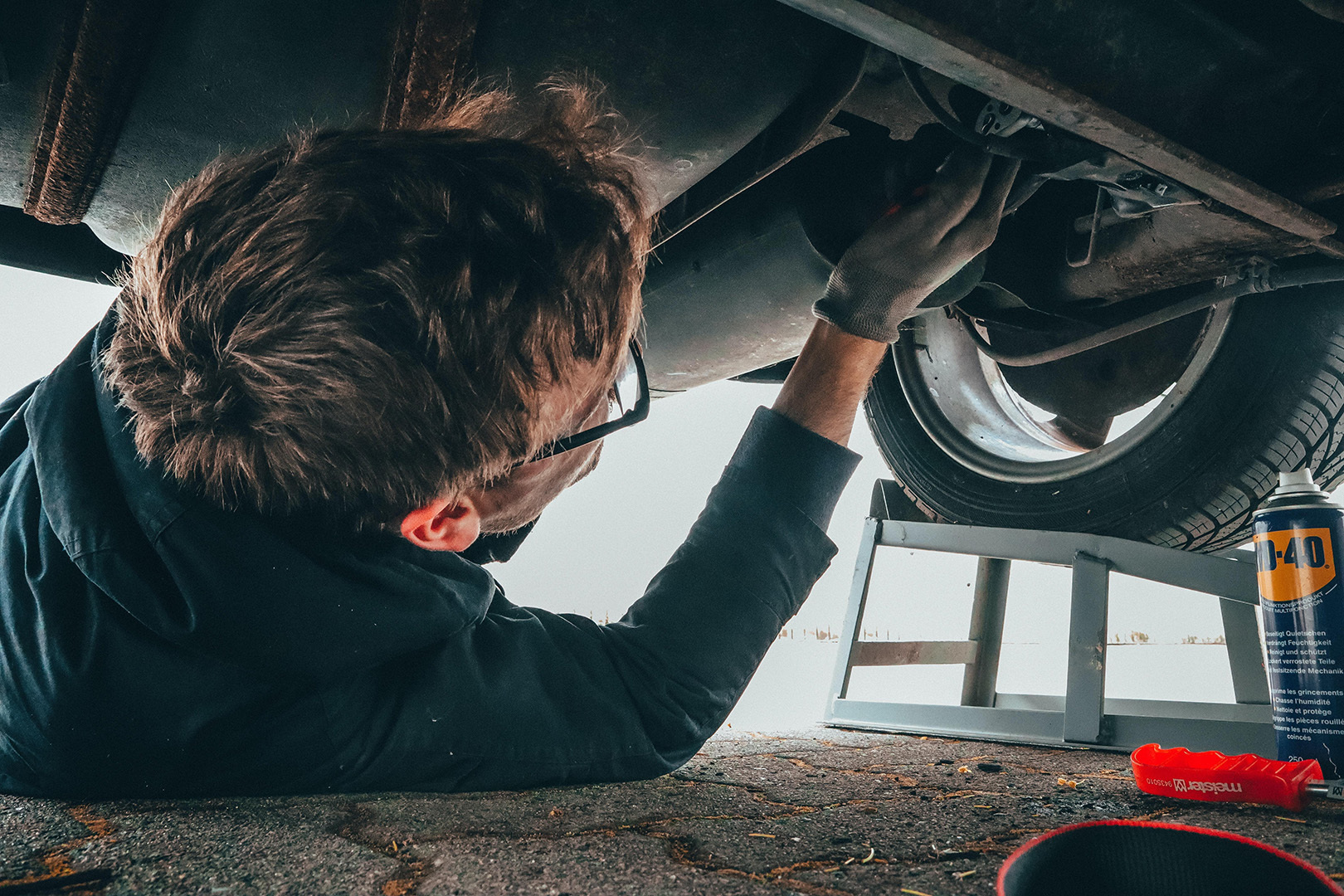 Mechanic working on the underside of a car, showcasing Fahrzeugtechnik Nink's expert vehicle maintenance services.